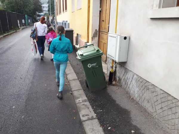 Gunoaiele pe trotuar, elevii printre maşini, pe stradă